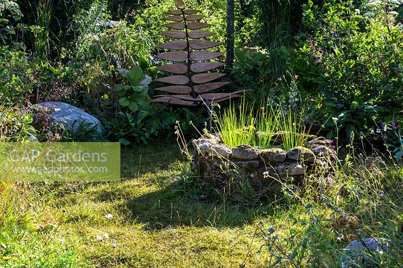 Sculptural bespoke garden chair made from recycled wood and metal, and drystone fire pit in a wild garden. Calm amidst Chaos. RHS Hampton Court Palace Flower Festival, 2019.  
