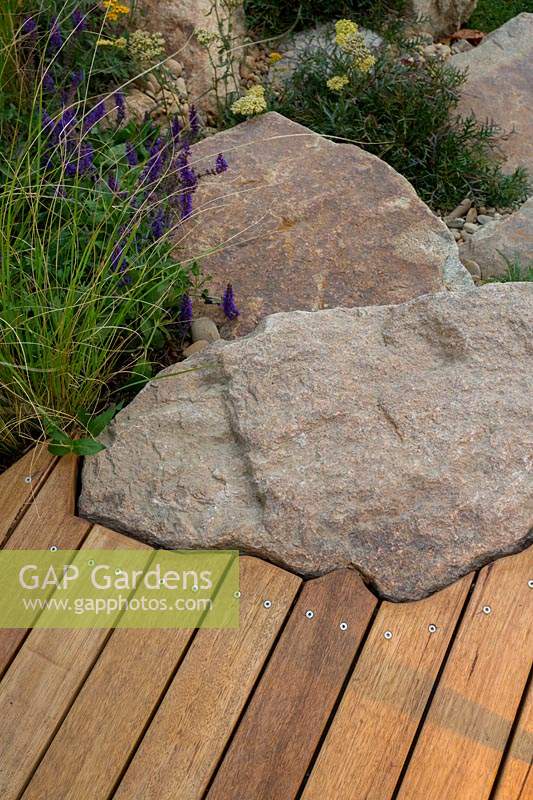 Detail of edging of a timber boardwalk that has been hand cut to conform the the shape of a rustic sandstone rock.