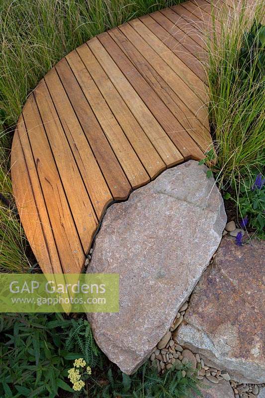 Detail of edging of a curved timber boardwalk that has been cut to conform to the shape of a rustic sandstone rock path.
