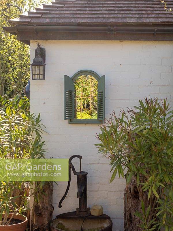 A mirror to replicate a window in a wooden green frame and increases the light in the garden and adds interest to the site wall. A vintage water pump in a barrel adds a touch of interest.