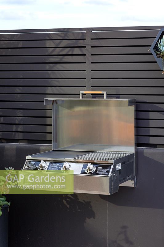 A small three burner barbecue mounted and a wall in a rooftop, patio garden.