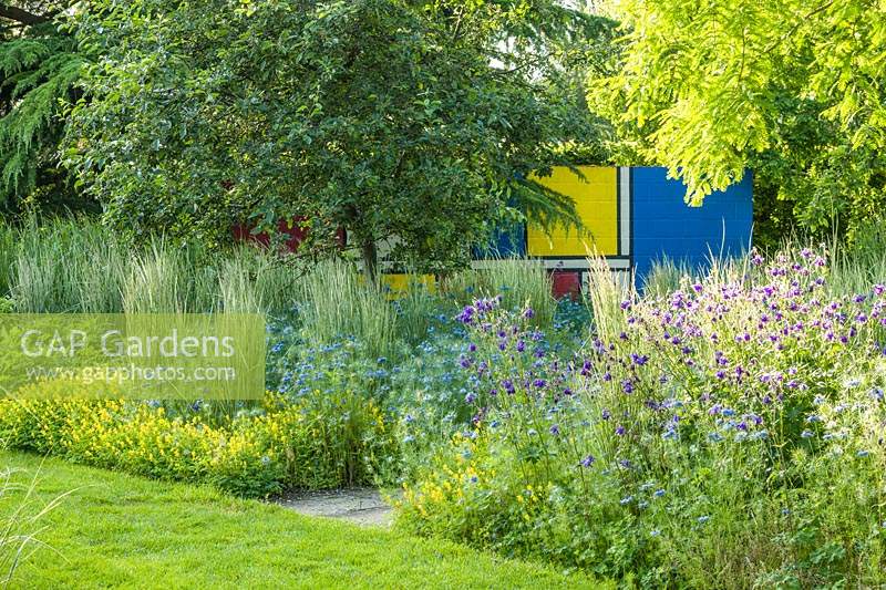 Summer borders with  Mondrian inspired painted wall in the background Planting includes Miscanthus sinensis 'Morning Light'