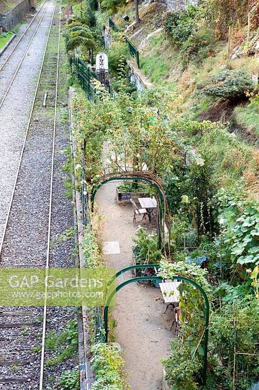 Metal arches supporting shrubs over a path running alongside railway tracks. Parc de Ruisseau, Paris