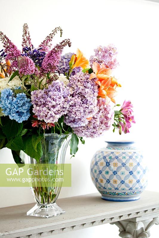 Glass vase on shelf with hydrangeas, lillies and buddleia
