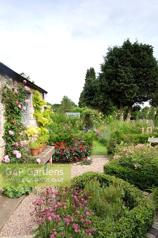 Small country cottage garden with parterre and gravel path leading to bench