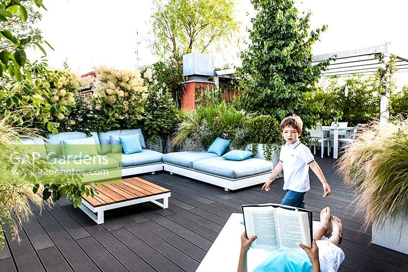 Overview of roof terrace with boy walking on deck and adult reading on a lounger