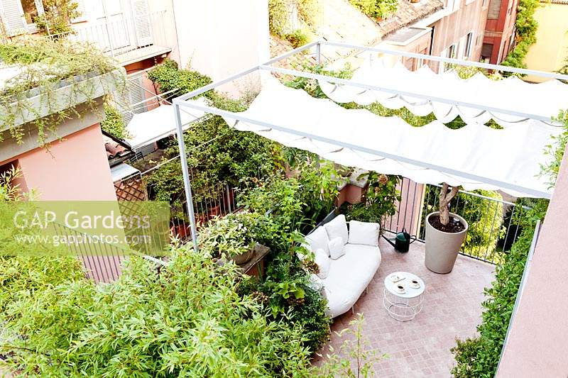 View of tiled terrace from the upper floor, showing shade canopy over seating area, railings and plant screening