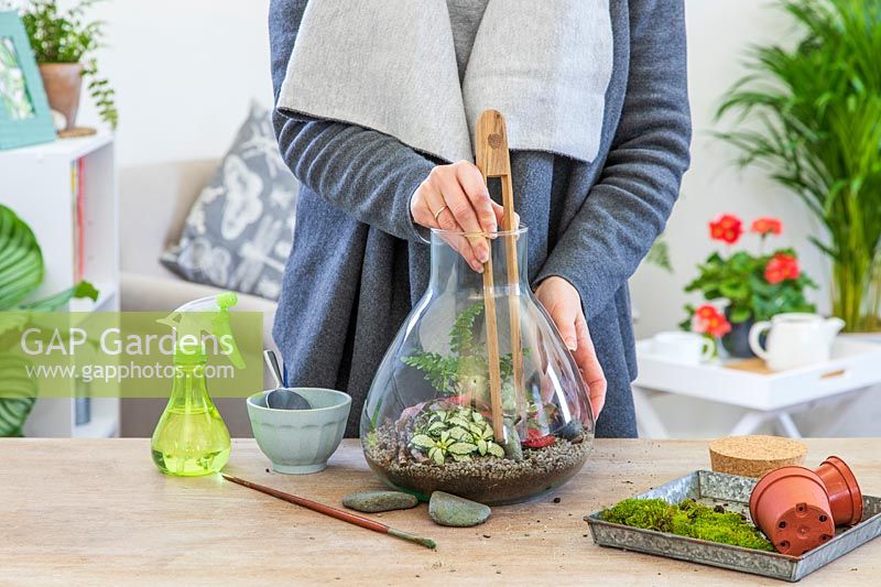 Woman using wooden tongs to place stones in a terrarium