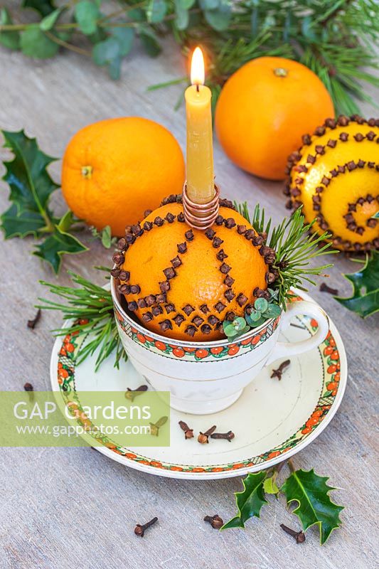Orange studded with cloves in teacup holding candle