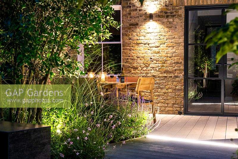 Illuminated dining area by the house surrounded by summer borders 