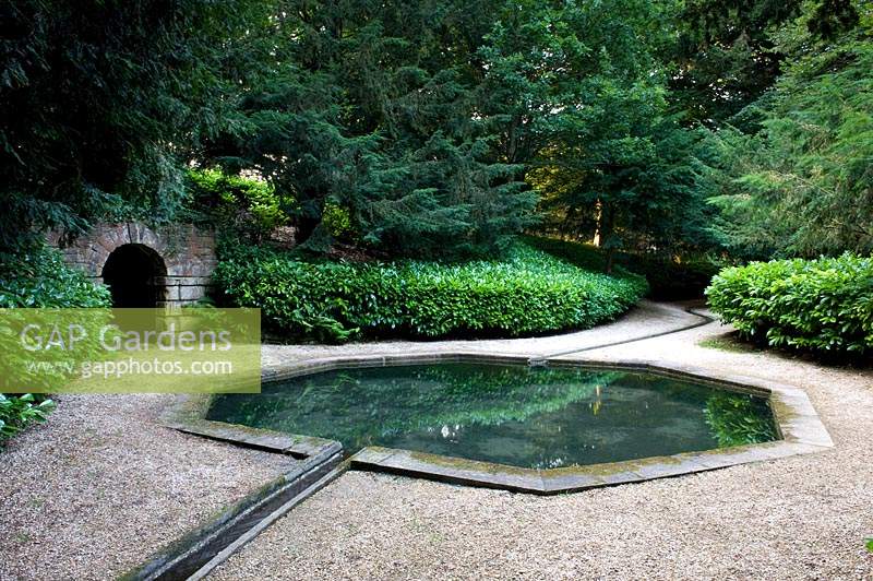 Gravel path leading around water feature pond and meandering water rill, stone tunnel set in wall