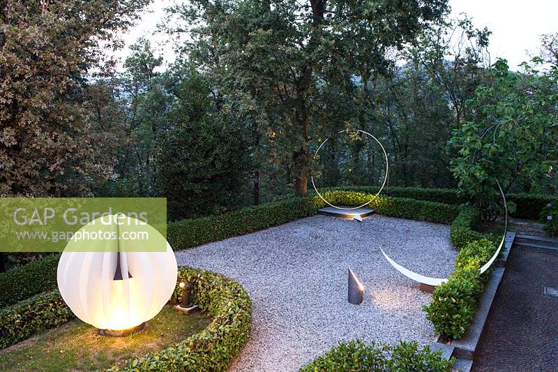 Landscape art with lighting, set on terrace with low hedging with trees beyond