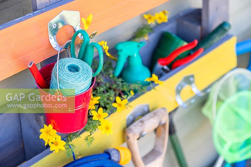 Close up detail of rainbow coloured pallet organiser holding  various garden tools