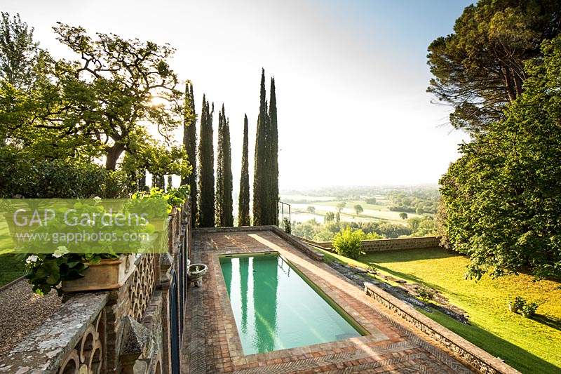 Overview of garden along terraces looking out on landscape, with swimming pool below and Cupressus sempervirens - Cypress - trees