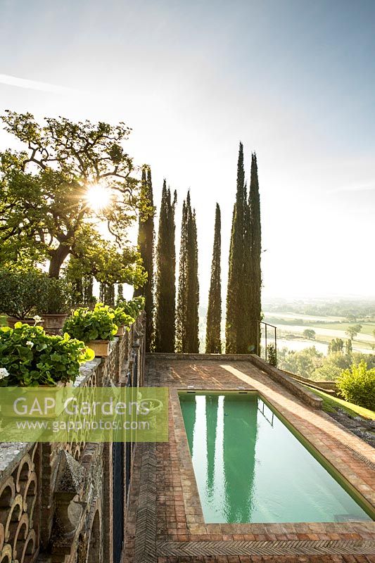 A swimming pool set in a terrace, views of Cupressus sempervirens - Cypress - trees and wider landscape 