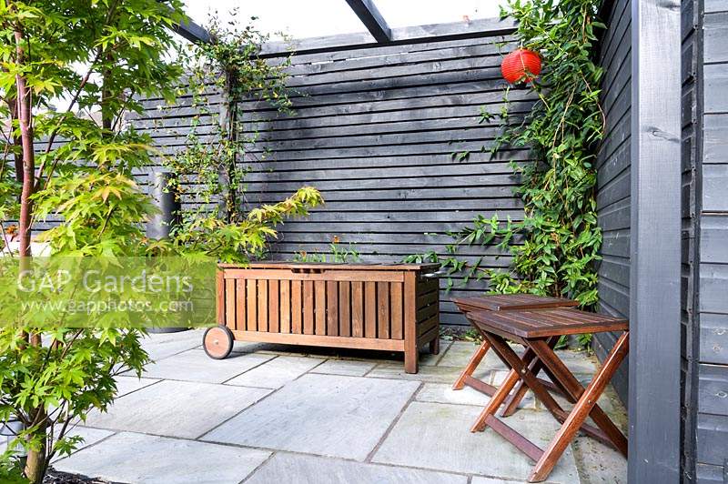 Modern Town Garden in Essex - black wooden pergola with mobile wooden storage and two stools.