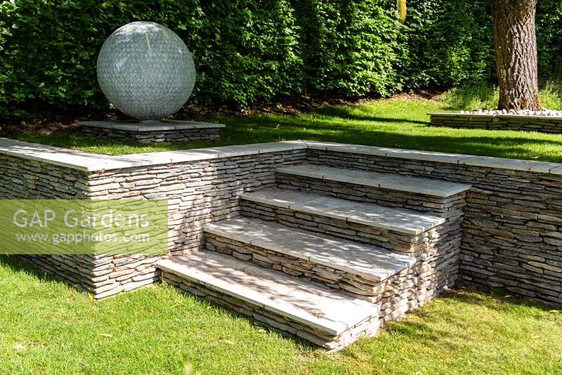 Raised garden with retaining granite wall and steps and large globe ornament