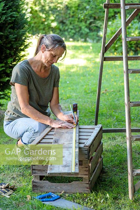 Woman measuring old floor boards to creae shelves for ladder unit