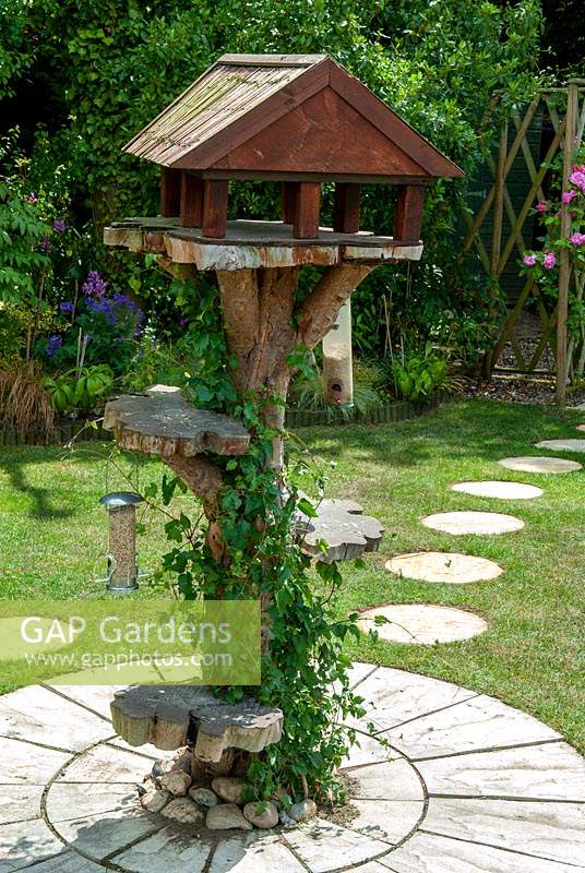 Rustic bird table with hanging feeders and feeding platform, set in paving in a lawn  - Open Gardens Day, Friston, Suffolk