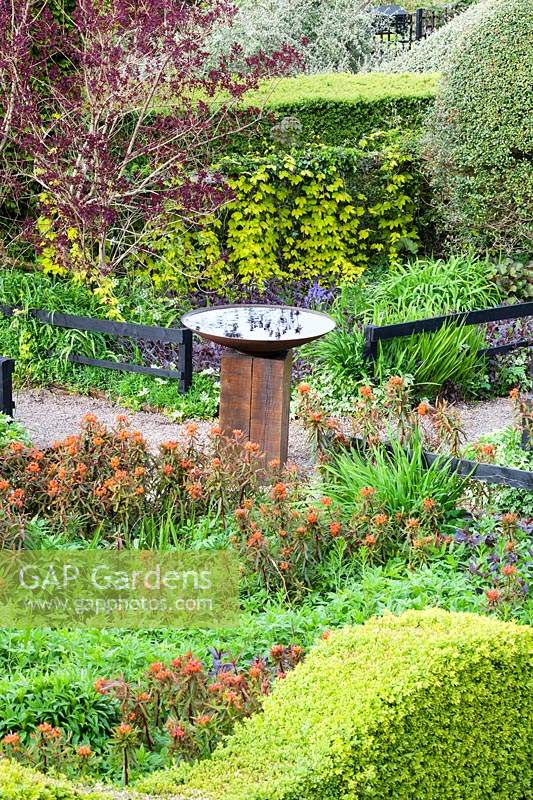 Central birdbath in centre of pathway, surrounded by flowering borders. Veddw House Garden, Monmouthshire, Wales, UK.
