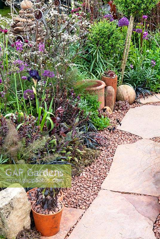 Stone path with granite chips alongside border of mixed plants and garden bric-a-brac - RHS Malvern Spring Festival