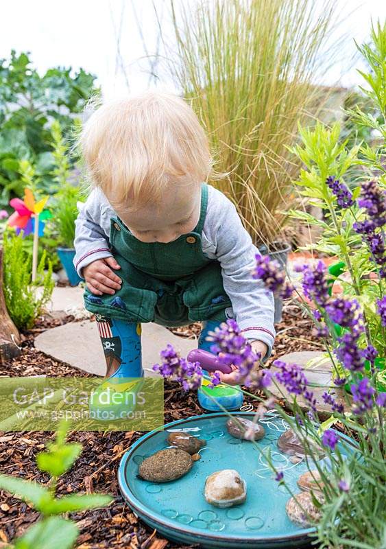 Young toddler playing with water and decorated stones in sensory garden