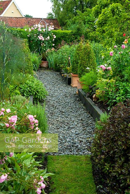 Raised beds and containers of herbs, shrubs and perennial plants, with path of slate chips leading to climbing pink rose  within metal obelisk - Open Gardens Day, Double Street, Framlingham, Suffolk