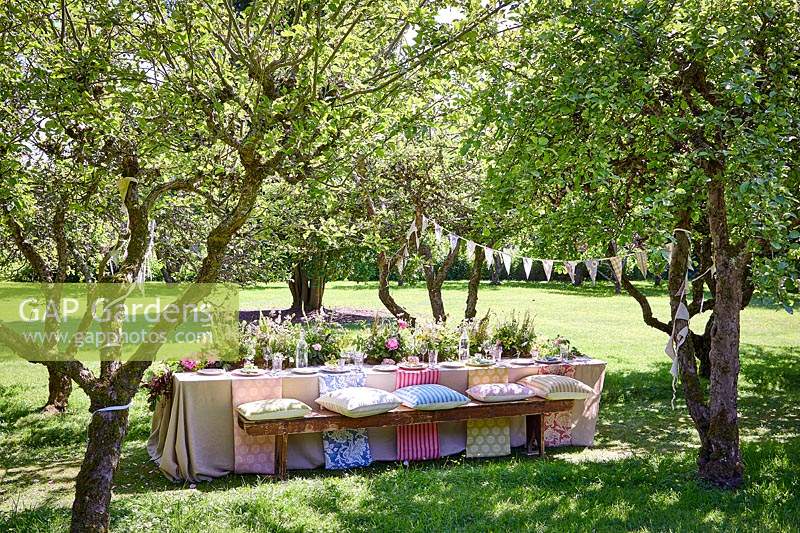Summer table setting in orchard with central floral arrangement and bunting 