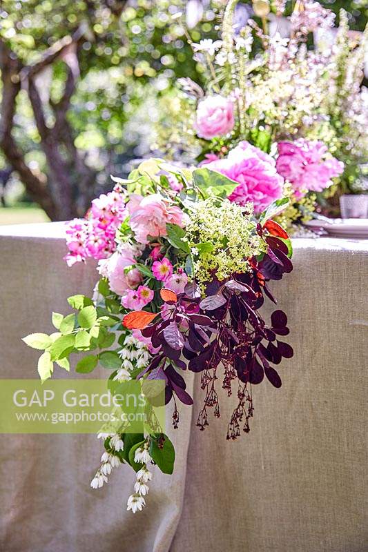 Floral arrangement hanging over the end of the table, flowers include roses, elderflower, Deutzia nad Cotinus