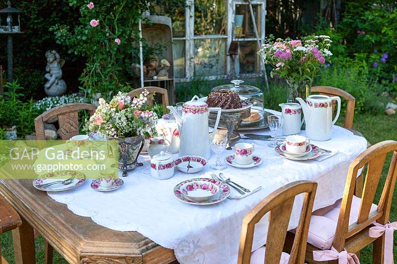 Romantic garden with laid table and wooden chairs