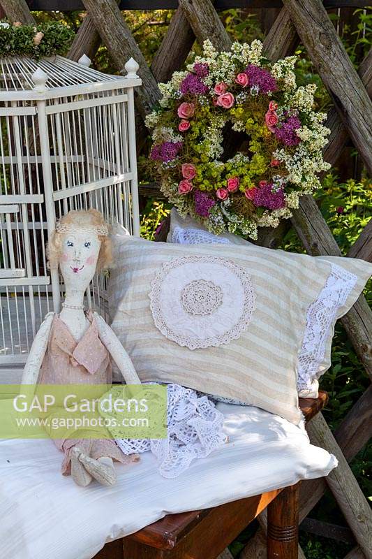 Floral wreath, bird cage, pillows and a rag doll on wooden table against a wooden lattice fence