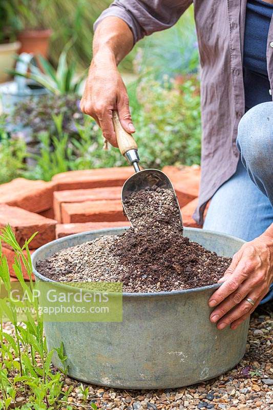 Woman using a scoop to mix grit and compost in galvanised container