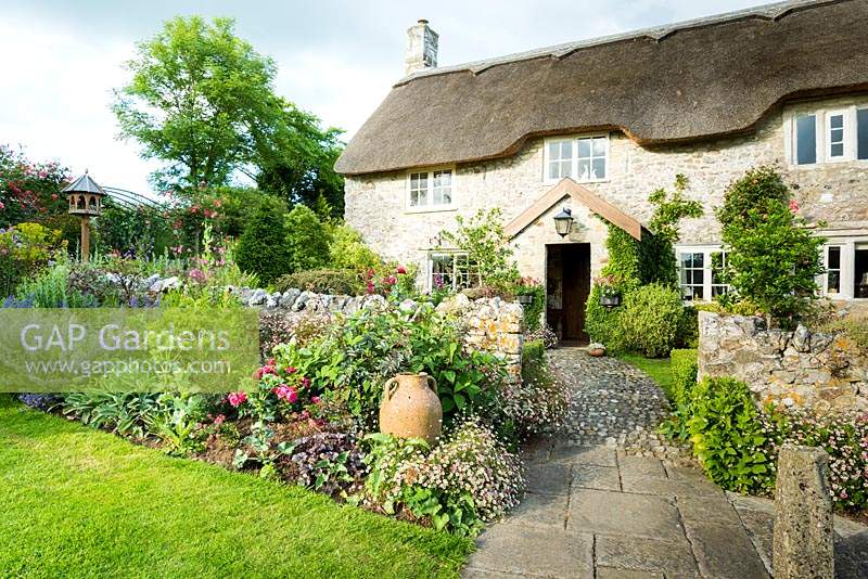 Thatched farmhouse framed by walls and lush planting including Erigeron karvinskianus, roses and catmint 