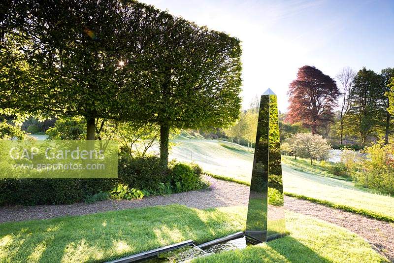 Stainless steel obelisk at the end of a rill framed by pleached hornbeams 
