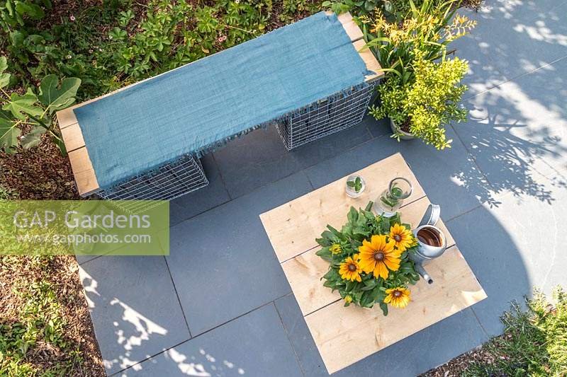 Overview of gabion and scaffolding board bench and table on slate patio in modern garden. 