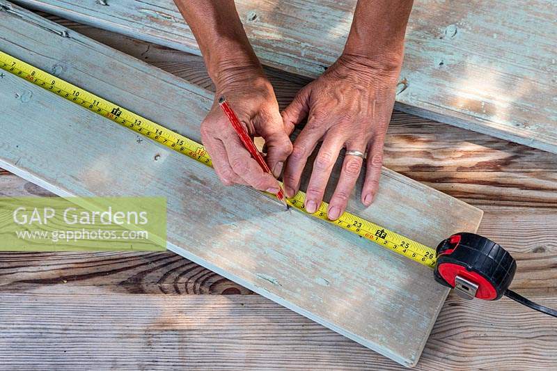 Woman measuring and marking where to cut the holes in the wooden boards. 