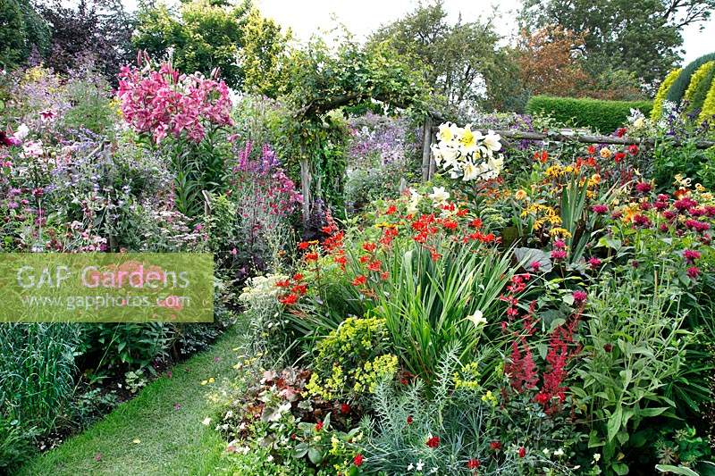 Packed flower beds, in foreground hot theme of red, yellow and purple flowers whilst beyond a bed of pink and purple flowers