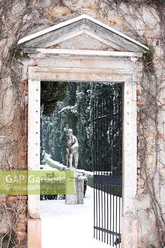View through open gateway to sculpture in snow covered formal garden