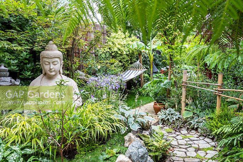 Buddha sculpture in small garden with exotic planting