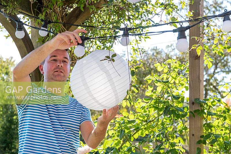 Man fixing white paper lantern over the bulbs in the light chain
