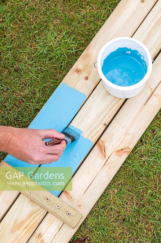 Man using a paintbrush to paint the wood before assembling the picnic bench