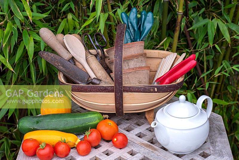 Trug with garden tools, teapot and freshly picked tomatoes, cucumber and courgette.