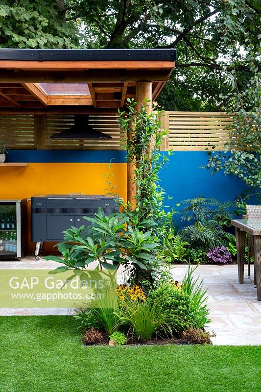 Patio and outdoor room with covered barbecue. Surrounded by a contemporary wooden trellis fence and blue painted wall.