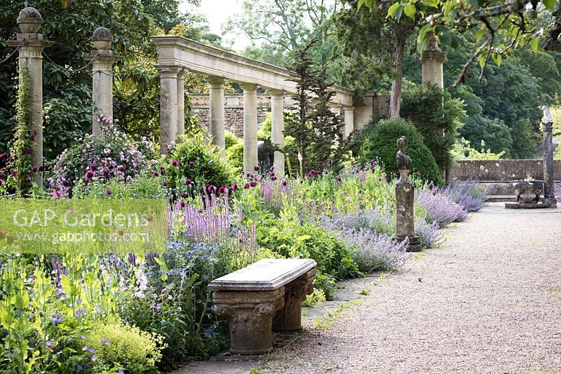 A border full of Papaver - Opium Poppy -  and Nepeta - Catmint - backed by a colonnade and surrounded by sculptural fragments 