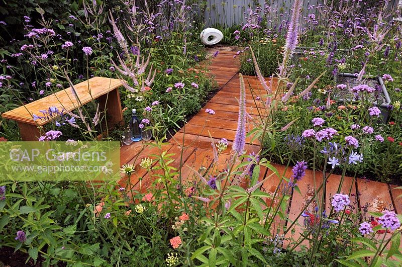 A path of wooden boards surrounded by colourful perennials leading to a contemporary Carrara marble sculpture. 'A Place to Think' garden by Southend Young Offenders'. 