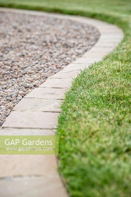 Path edge made from square pavers, edging between lawn and gravel path. 