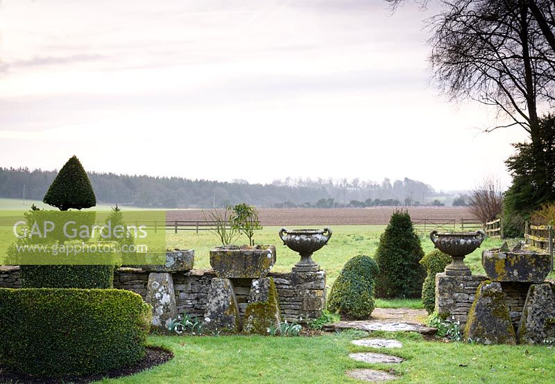 Pair of classic urns displayed on stone wall in the Topiary garden, with views out to surrounding fields at Rodmarton Manor, Glos, UK. 