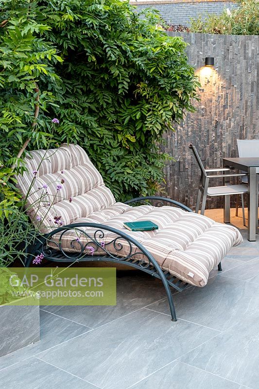 Wide decorative sun lounger with cushion backed by Wisteria, wall-mounted downlighter