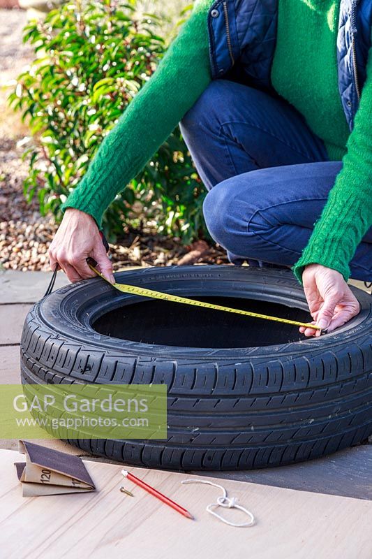 Woman using measuring tape to measure width of car tyre
