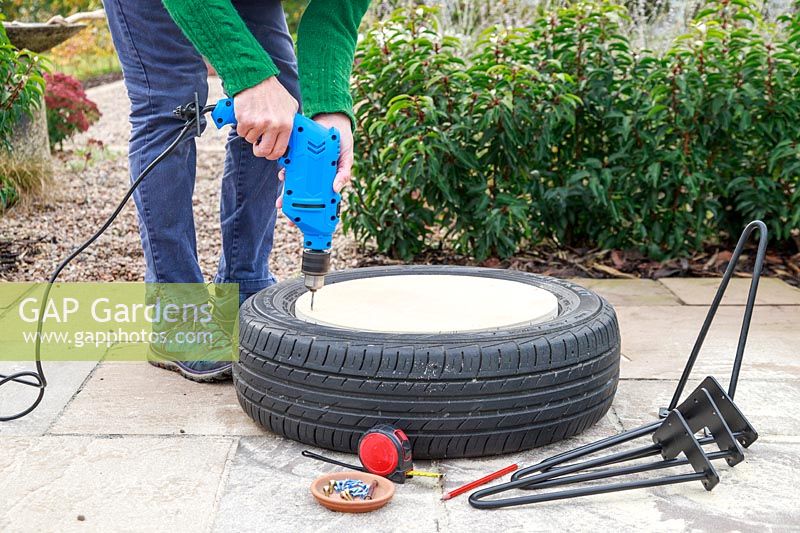 Woman using an electric drill to make pilot holes through plywood disk into car tyre